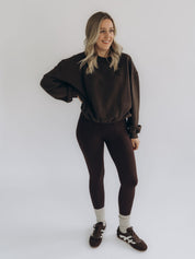 Michi trägt den dunkelbraunen Sweater LAURA 2.0 in einer frontalen Ganzkörperansicht.