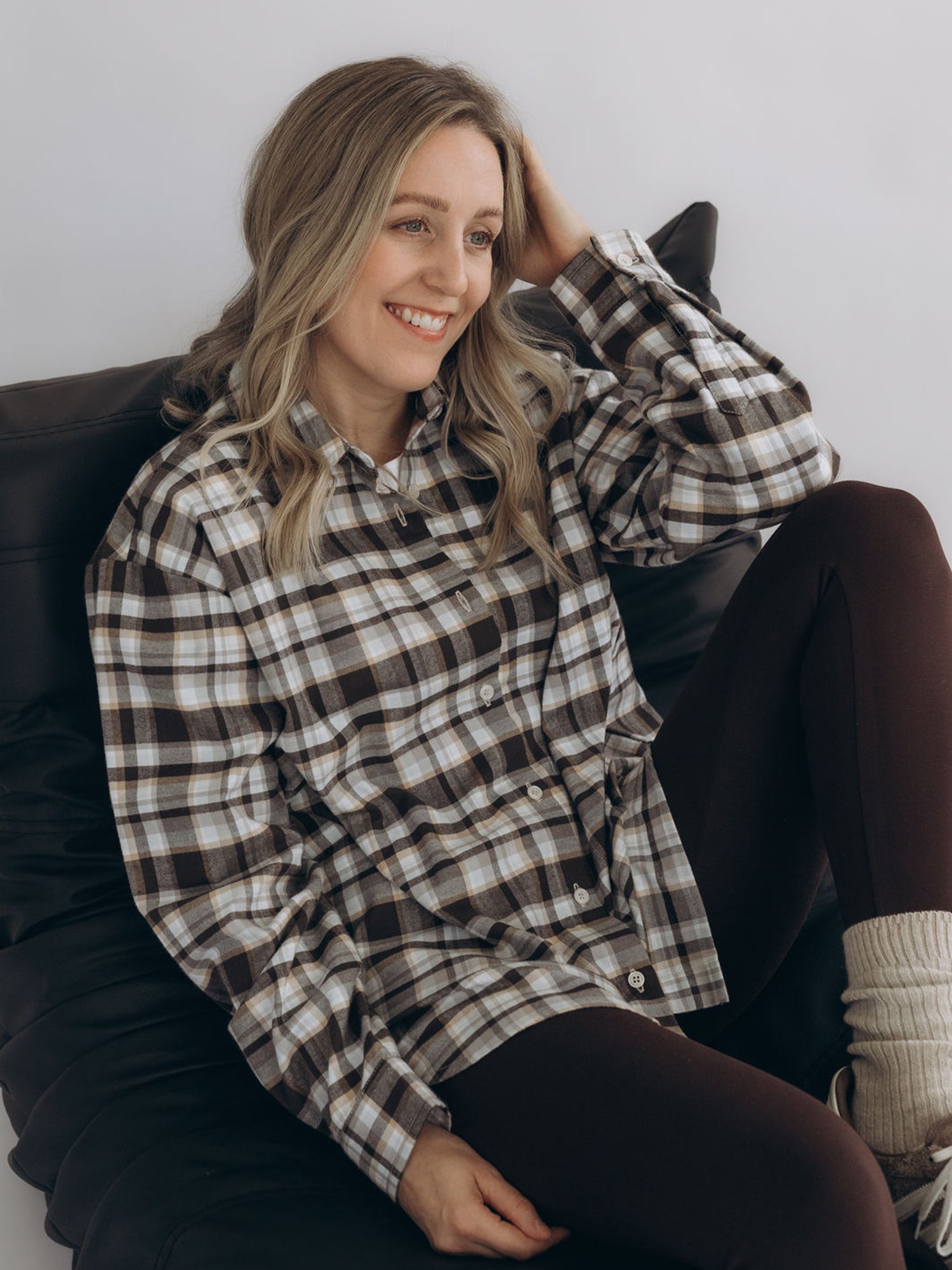 Michi trägt das Flanellhemd BERTHA in Check Brown in einer sitzenden Halbansicht mit lockerem Oversized-Sitz