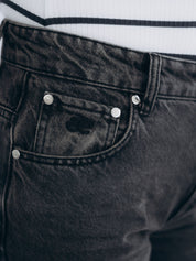 Detailaufnahme von Bund, Knopfverschluss und vorderen Taschen im verwaschenen dunkelgrauen Denim. Everless Signé eingestickt.