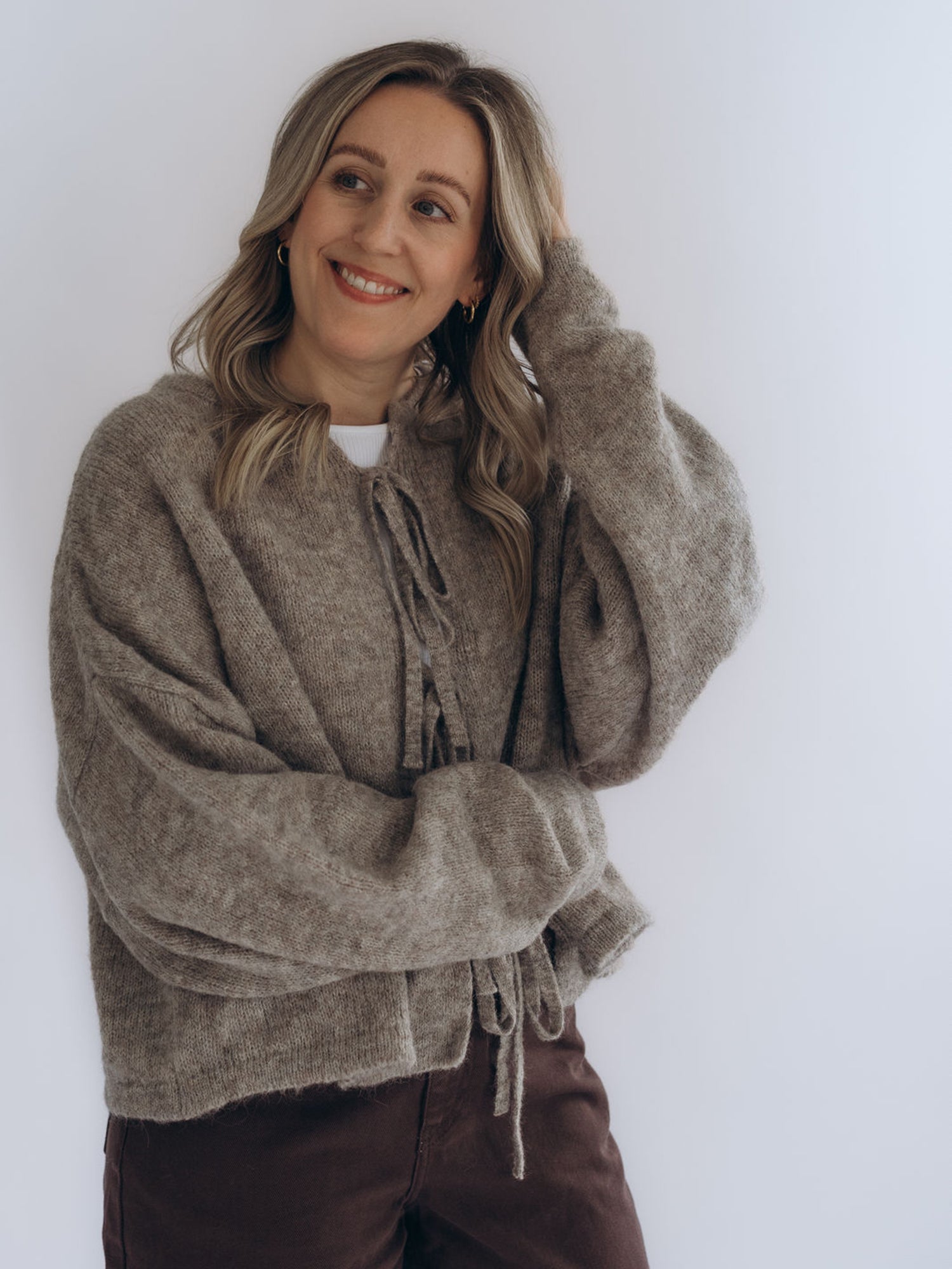 Michi trägt die Strickjacke ANNELIESE in Sandy Beige in einer frontalen Halbansicht mit lockerem Sitz.