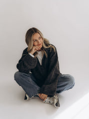 GRETA in einer sitzenden Ganzkörperansicht; der lockere, hüftlange Oversized-Schnitt ist sichtbar