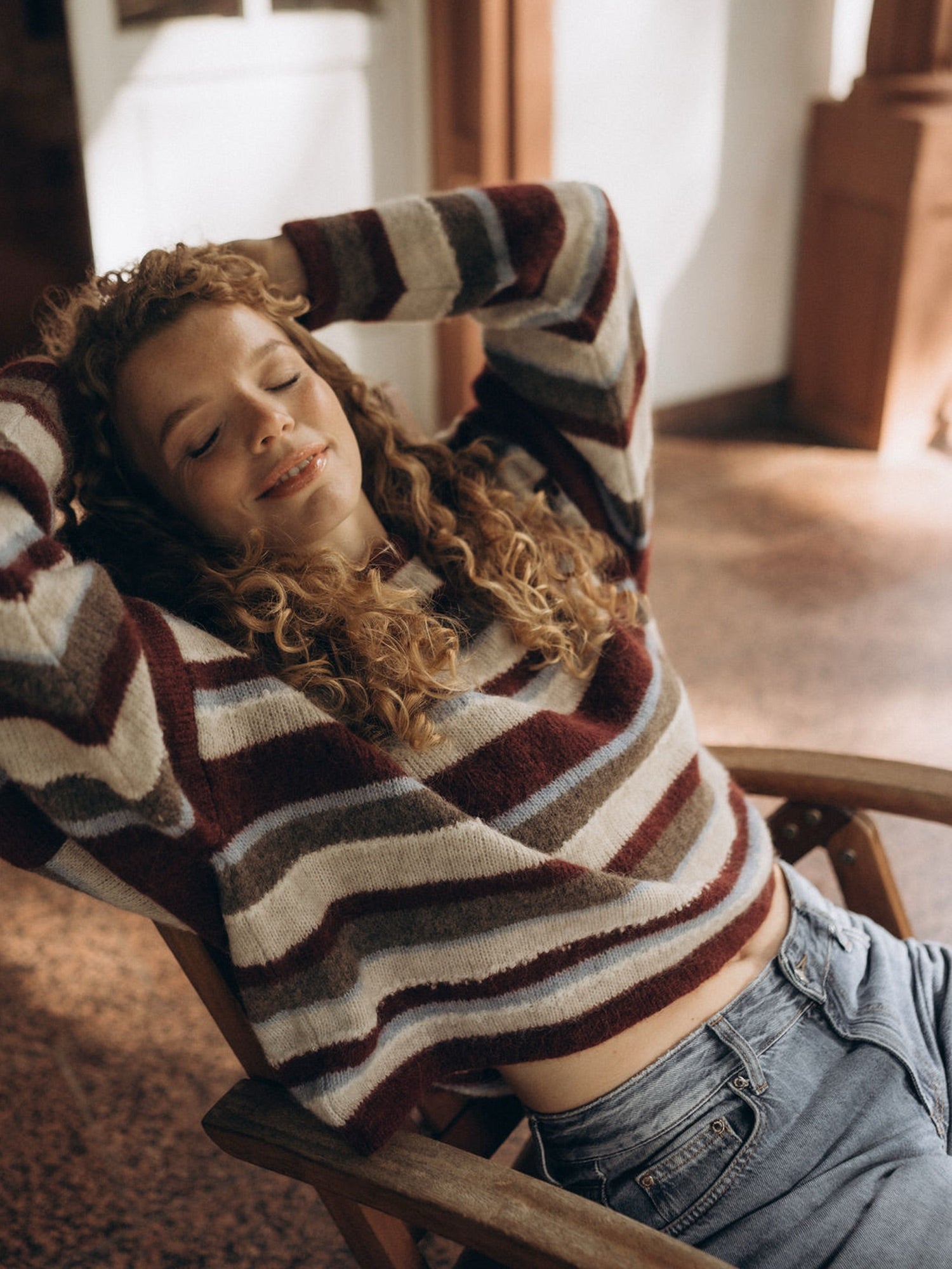 Unser Model Kathi trägt den gestreiften Strickpullover IRA entspannt in einem warm beleuchteten Innenraum.