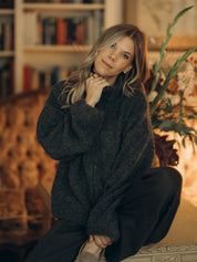 Lena trägt die anthrazitfarbene Zipperjacke GRETA sitzend in einem warm beleuchteten Wohnraum.