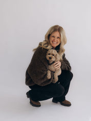 Angi trägt TILDA hockend zu einer schwarzen Hose MARIE flared und hält einen kleinen Hund im Arm